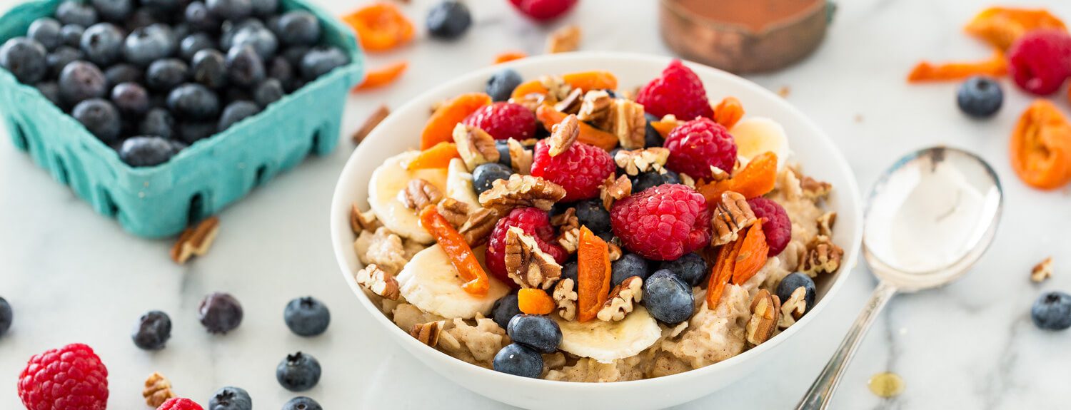  A bowl of oatmeal topped with fresh blueberries, raspberries, apricots, and walnuts, served with a side of honey.