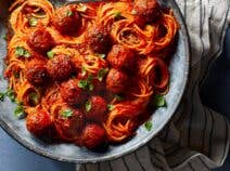 Big plate of vegan spaghetti with vegan meatballs and red sauce served in gray-blue bowl and table