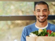 Portrait of a happy young man holding a bag full of healthy vegetables at home