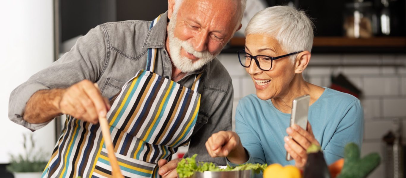 Man and woman cooking while following instructions on a smart phone.