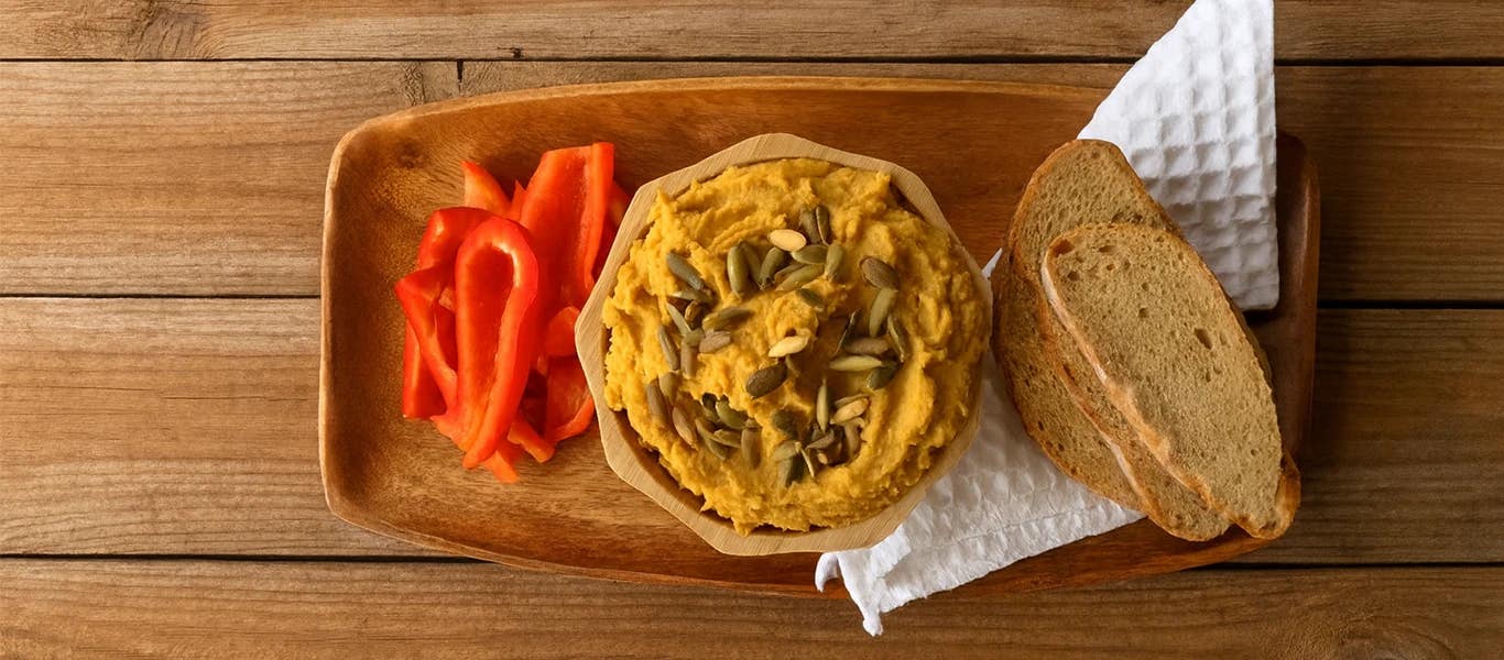 Pumpkin Hummus on a wooden serving platter with sliced red bell peppers and slices of crusty bread