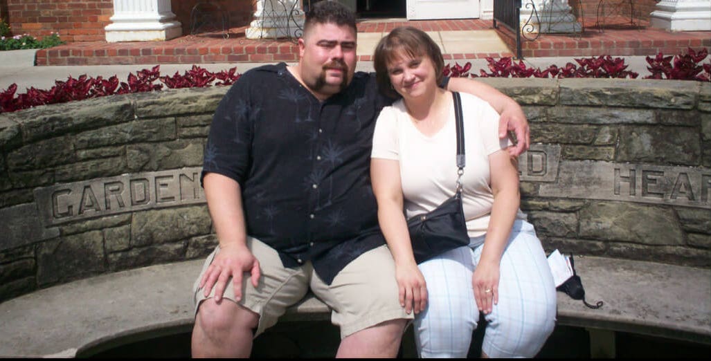 Tim Kaufman and his wife sitting arm in arm on a stone garden bench
