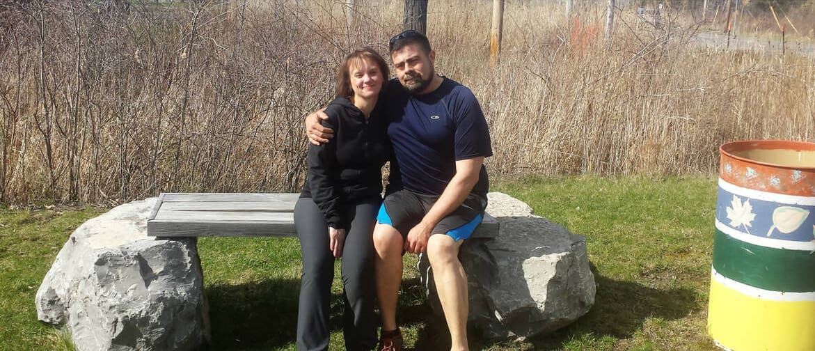 Tim Kaufman and his wife on a stone bench looking fit and happy