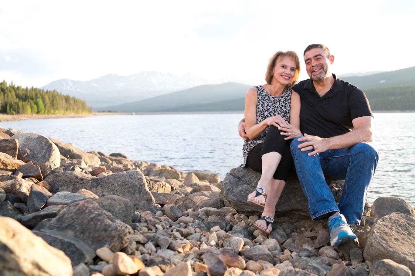 Tim Kauffman and his wife sitting on rocks with a stunning lake behind them