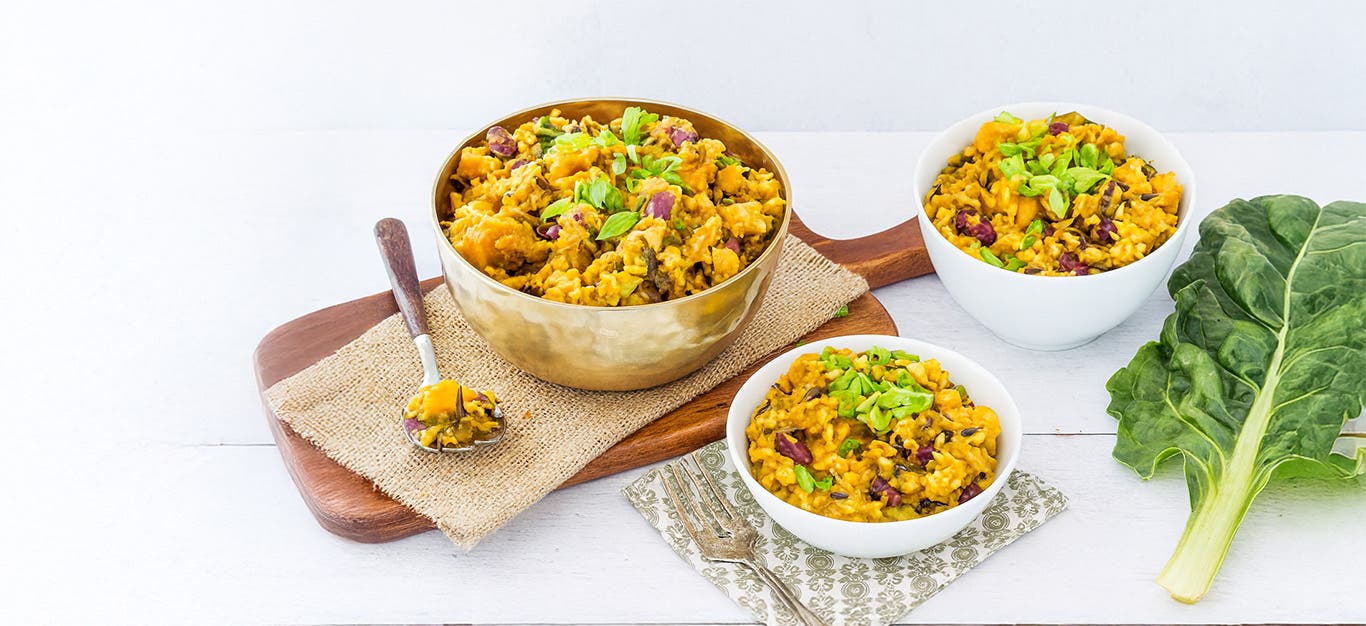 A large bowl of Caribbean Rice on a wooden chopping board next to two smaller bowls