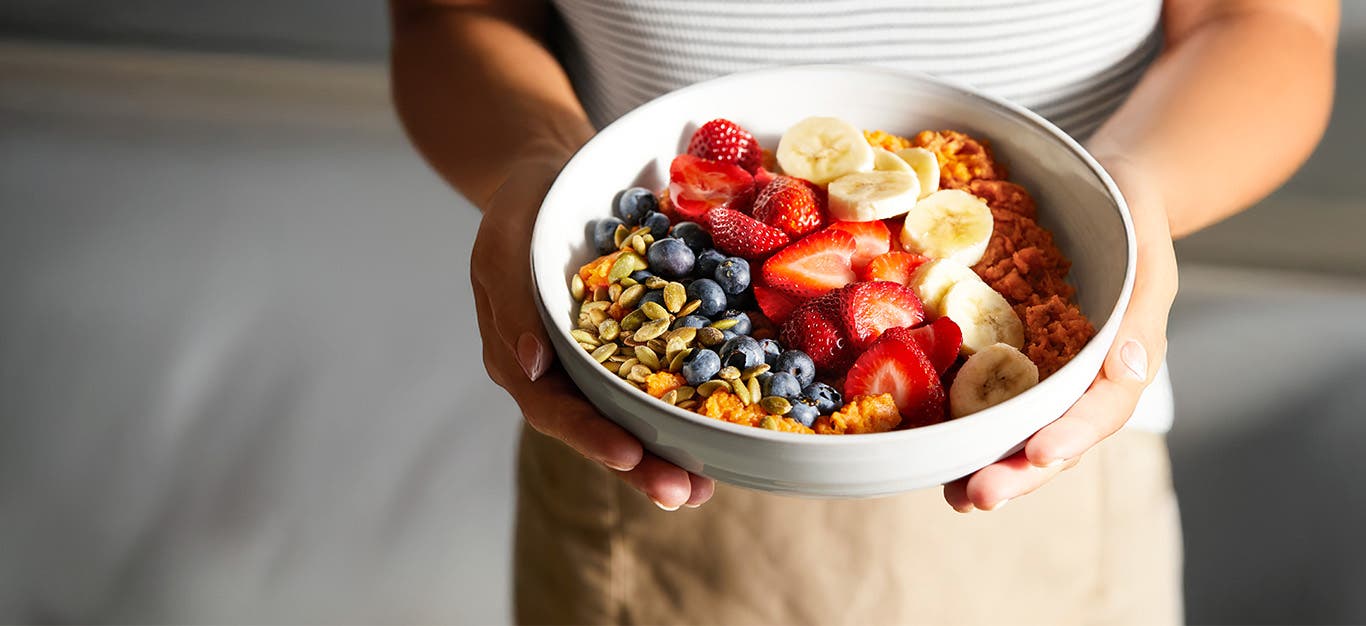 A woman holding a Rainbow Sweet Potato Breakfast Bowl with two hands