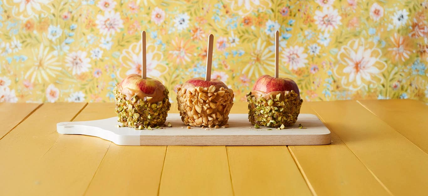 three vegan caramel apples dipped in nuts on a yellow background