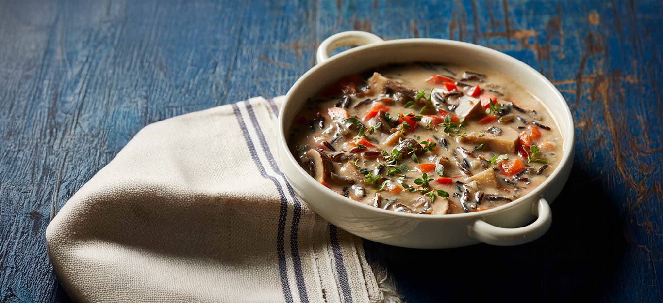 Creamy Wild Rice Soup in a wide-rimmed white bowl on a rustic blue wooden counter