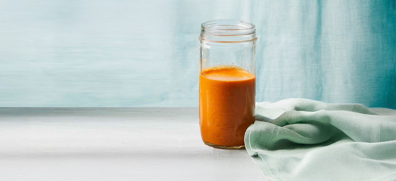 Vegan Queso Sauce in a glass jar, with a pale blue curtain in the backgroujd