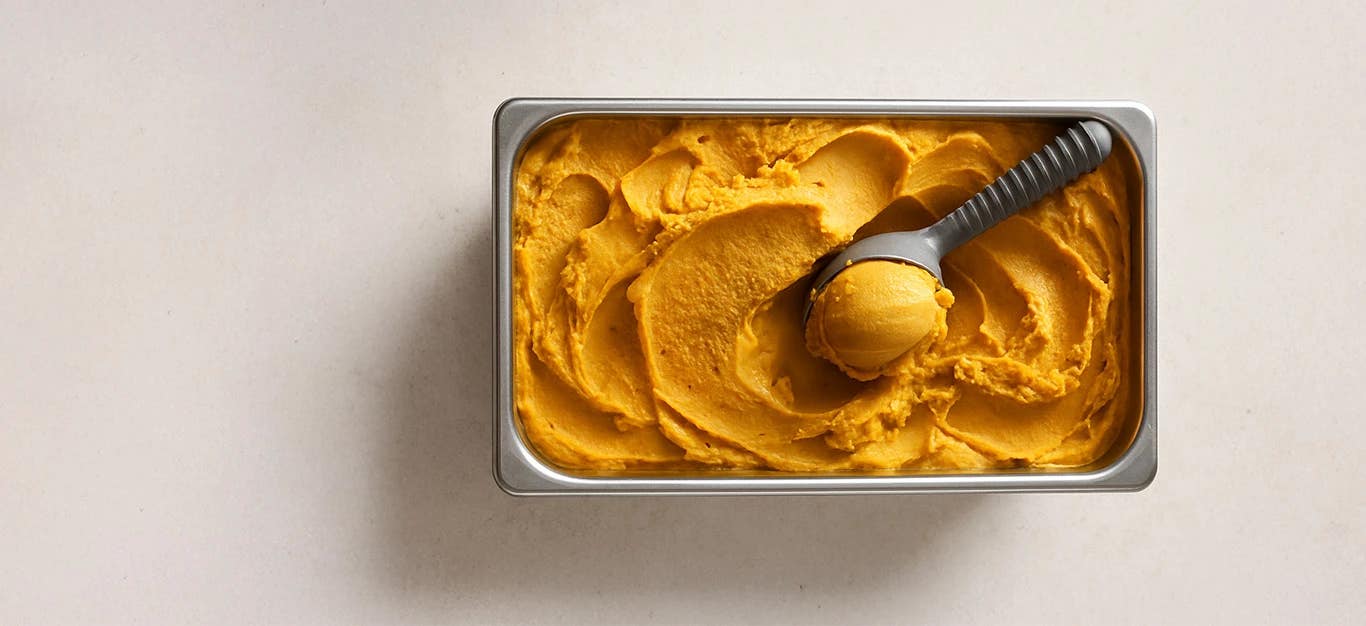A stainless tray of pumpkin ice cream with ice scoop