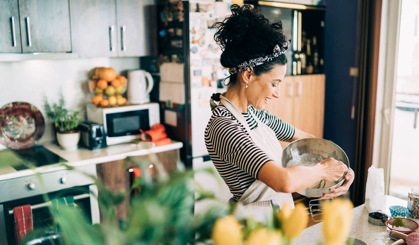 A bright image of a woman stirring batter in the kitchen, looking happy
