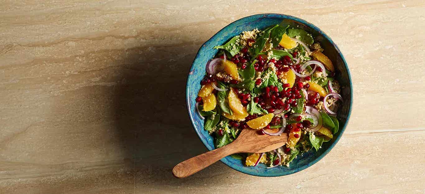 Date and Orange Couscous Salad in a blue ceramic bowl with a wooden spoon in the bowl