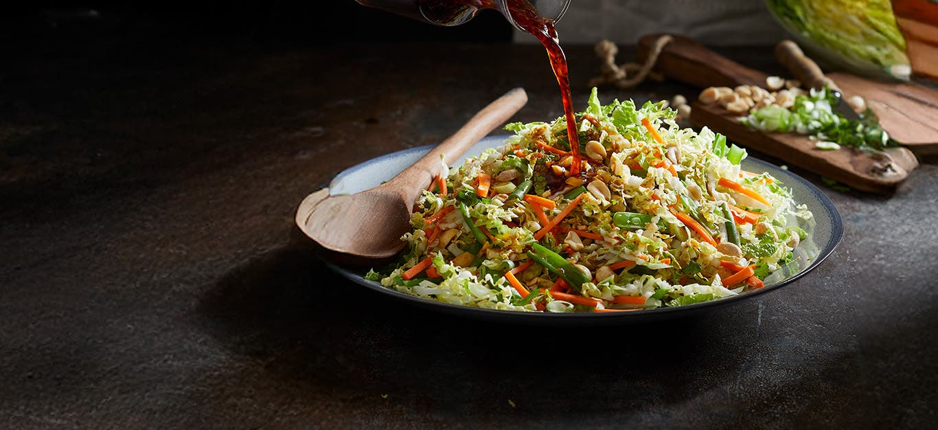 Coleslaw made with Napa cabbage in a serving bowl with dressing being poured over the top