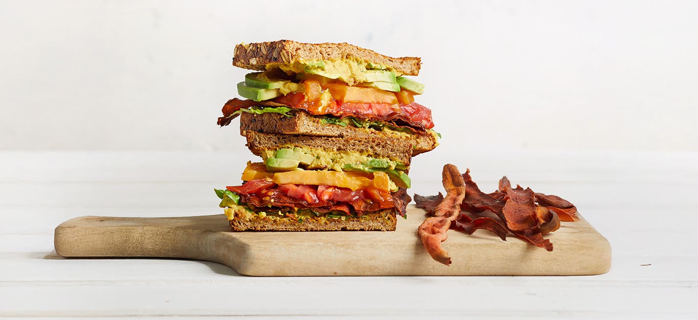 Vegan BLTA wit Carrot Bacon on a wooden chopping board against a white background