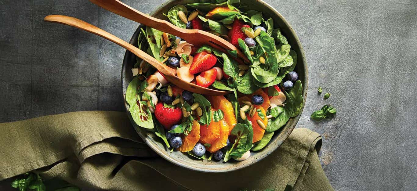 Sweet Spinach and Berry Salad in a green ceramic serving bowl with wooden tongs