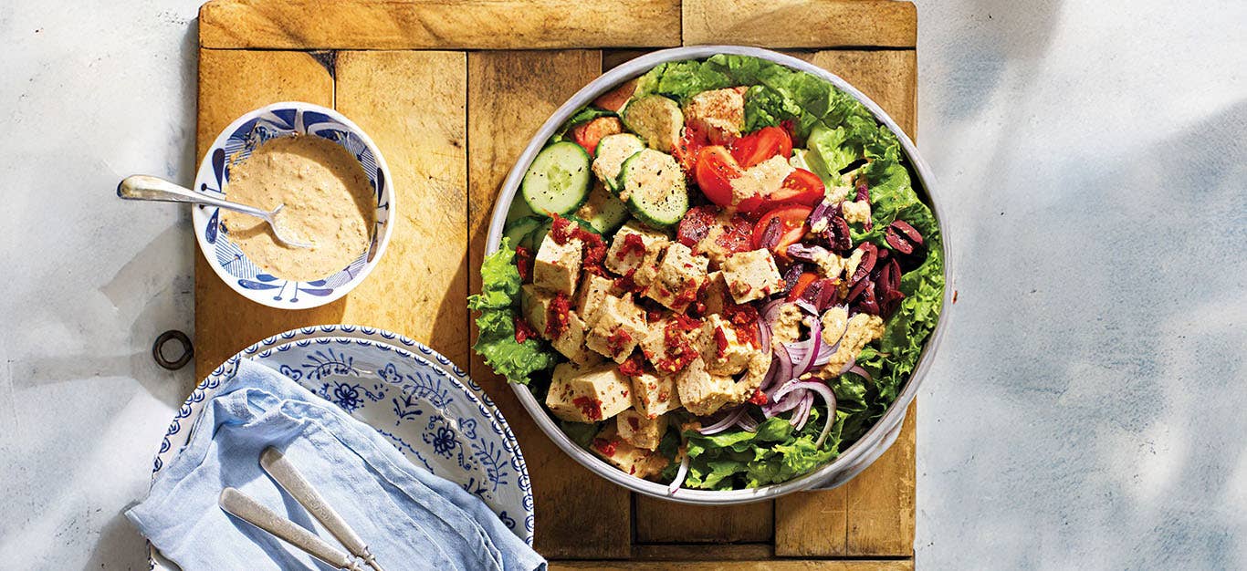 Greek Salad with Sun-Dried Tomato Tofu Feta in a serving bowl on a wooden chopping board