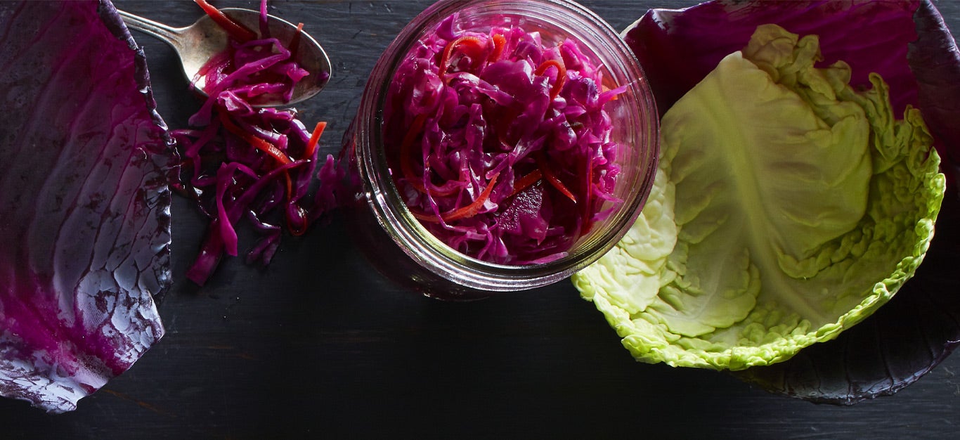 Spicy Red Cabbage Sauerkraut in a mason jar next to leaves of red and green cabbage
