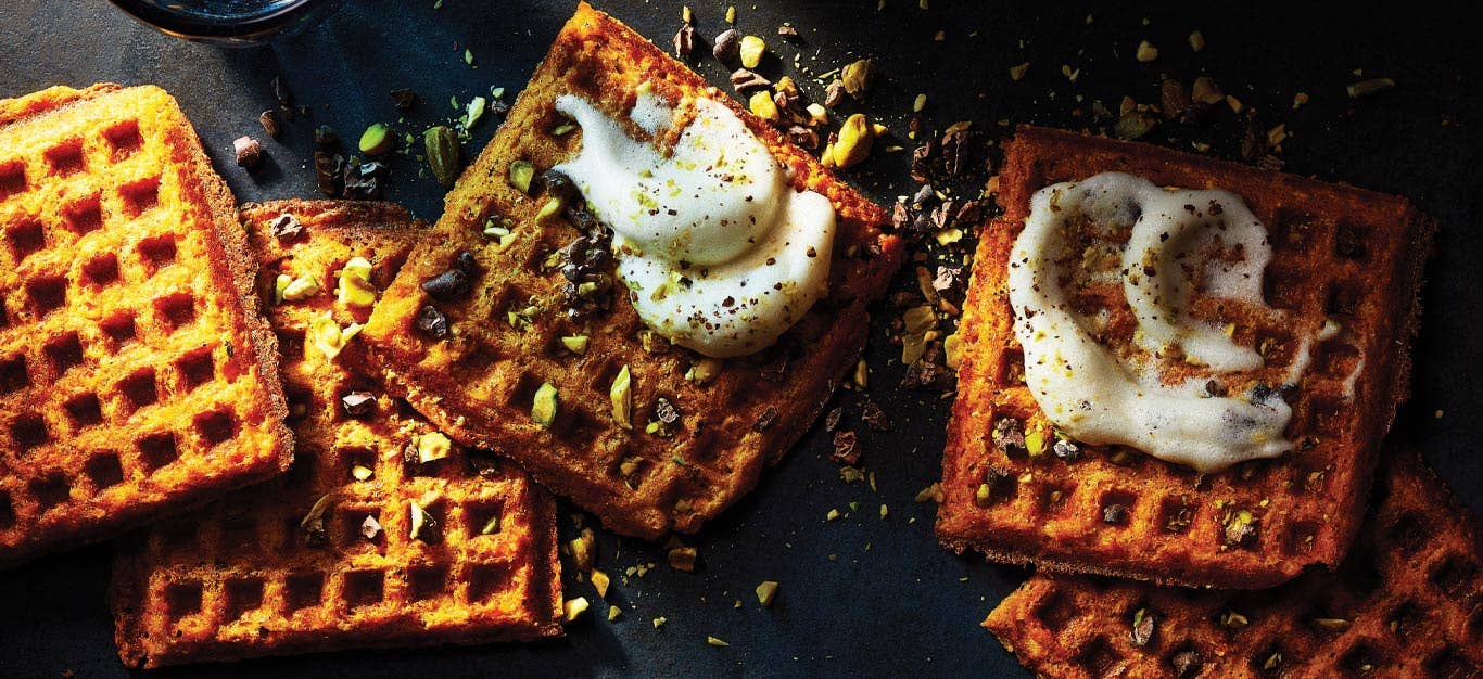 Sweet Potato Dessert Waffles topped with crushed nuts and whipped cream placed on a dark background