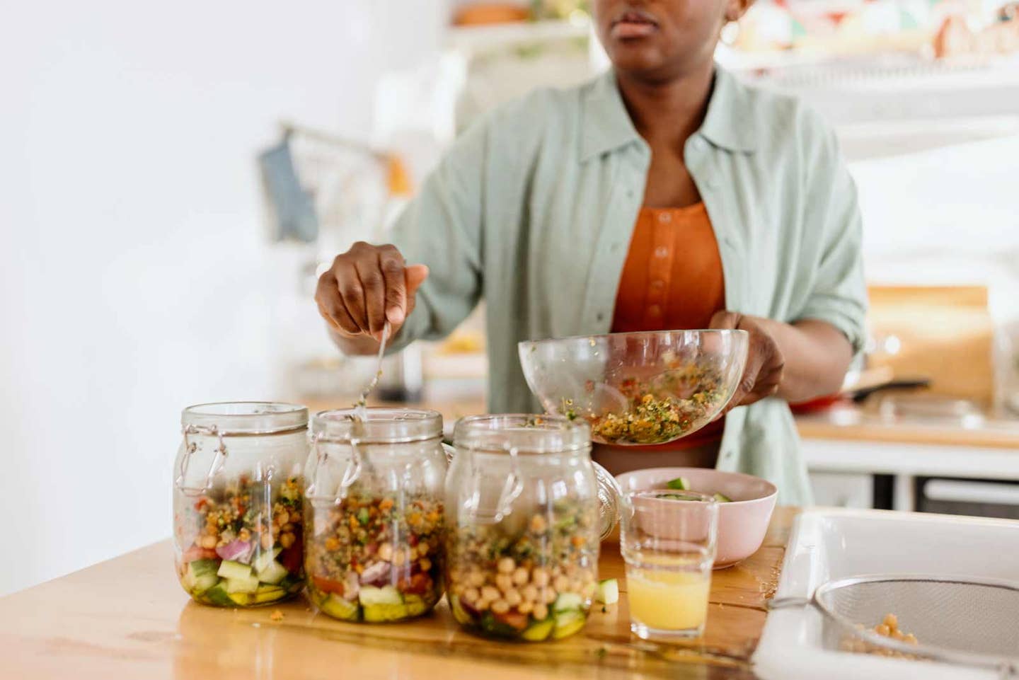 African American woman spooning chickpeas into mason jars holding meal prep salads