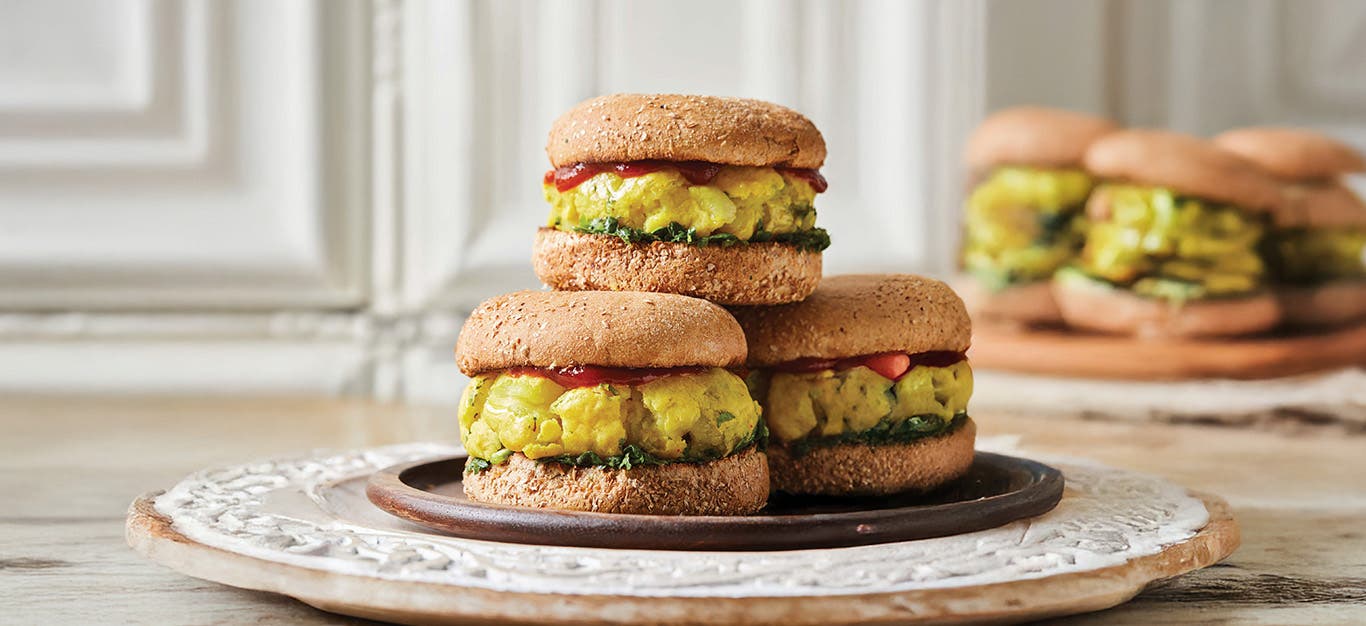 Three Bombay Potato Burgers on a plate, with another plate of burgers in the background