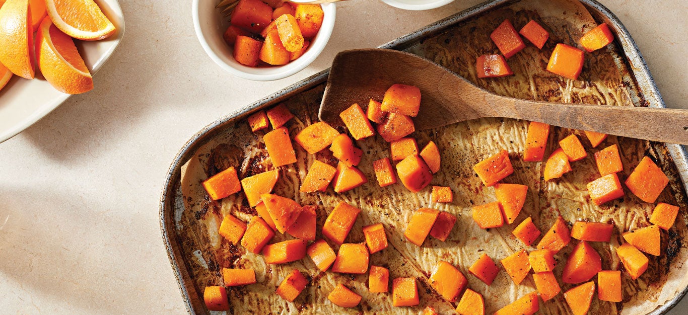 Butternut Squash with Orange Glaze on a baking sheet with a wooden spatula