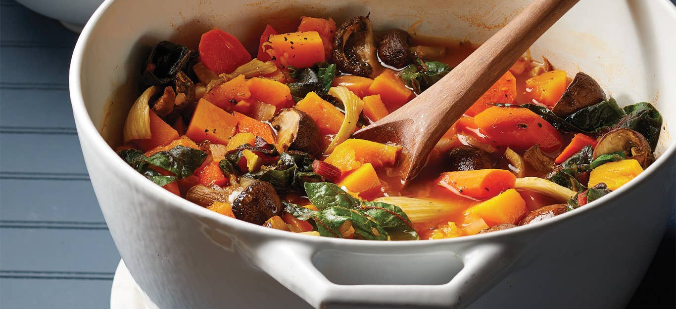 Roasted Kabocha Squash and Veggie Stew in a white Dutch oven with a wooden stirring spoon