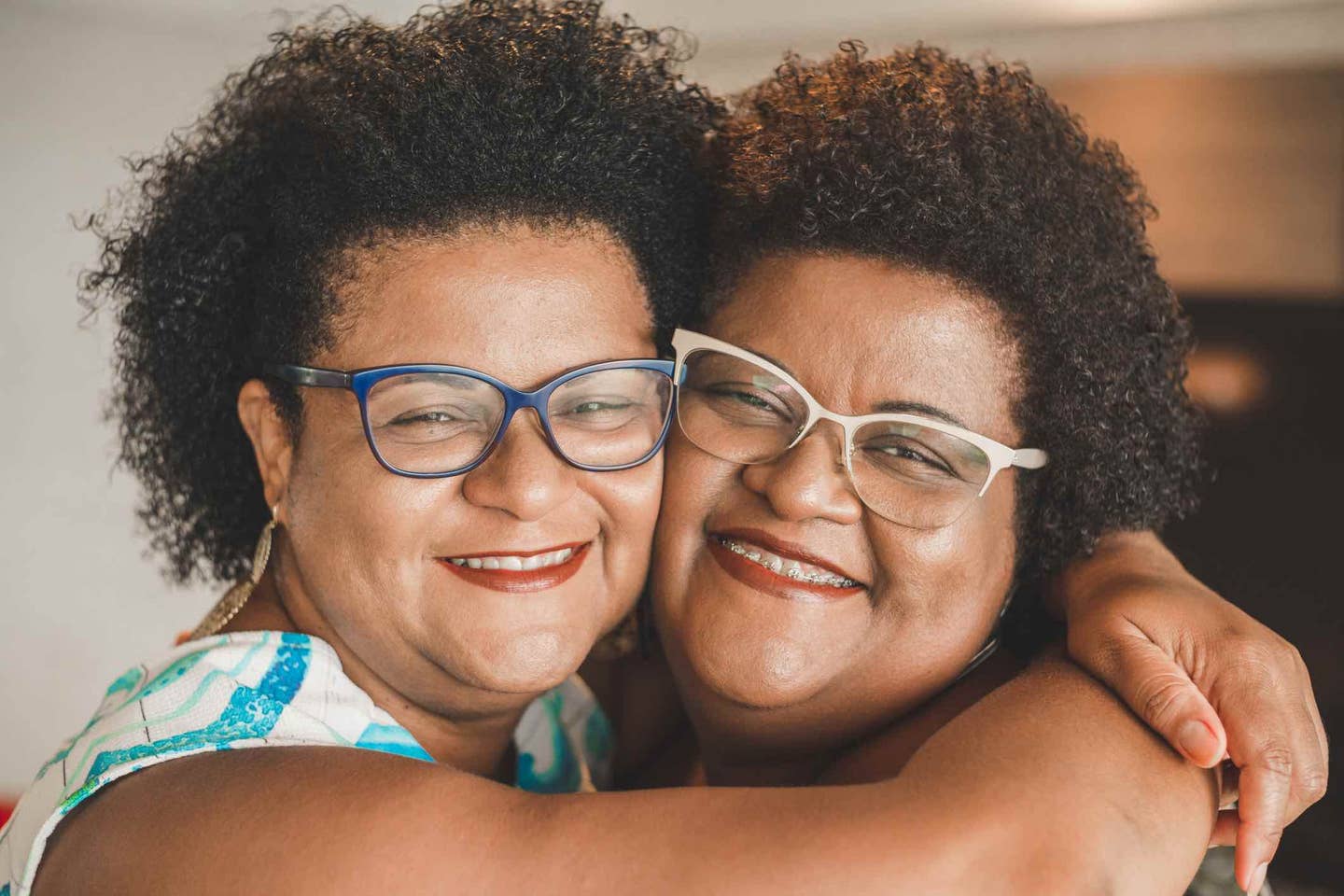 Happy twin sisters who are Black and both wearing glasses hugging, cheek to cheek