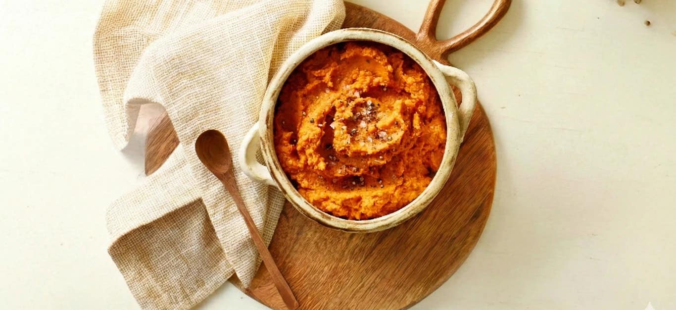 Harissa Hummus in a handmade ceramic bowl with a wooden spoon and beige tea towel to the side