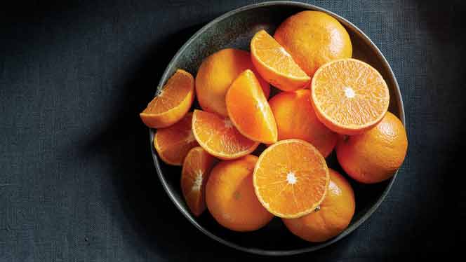 whole and sliced tangerines in gray ceramic bowl against a dark gray background