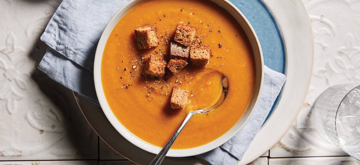 Root Vegetable Bisque with Whole Grain Croutons in a white bowl with a metal spoon