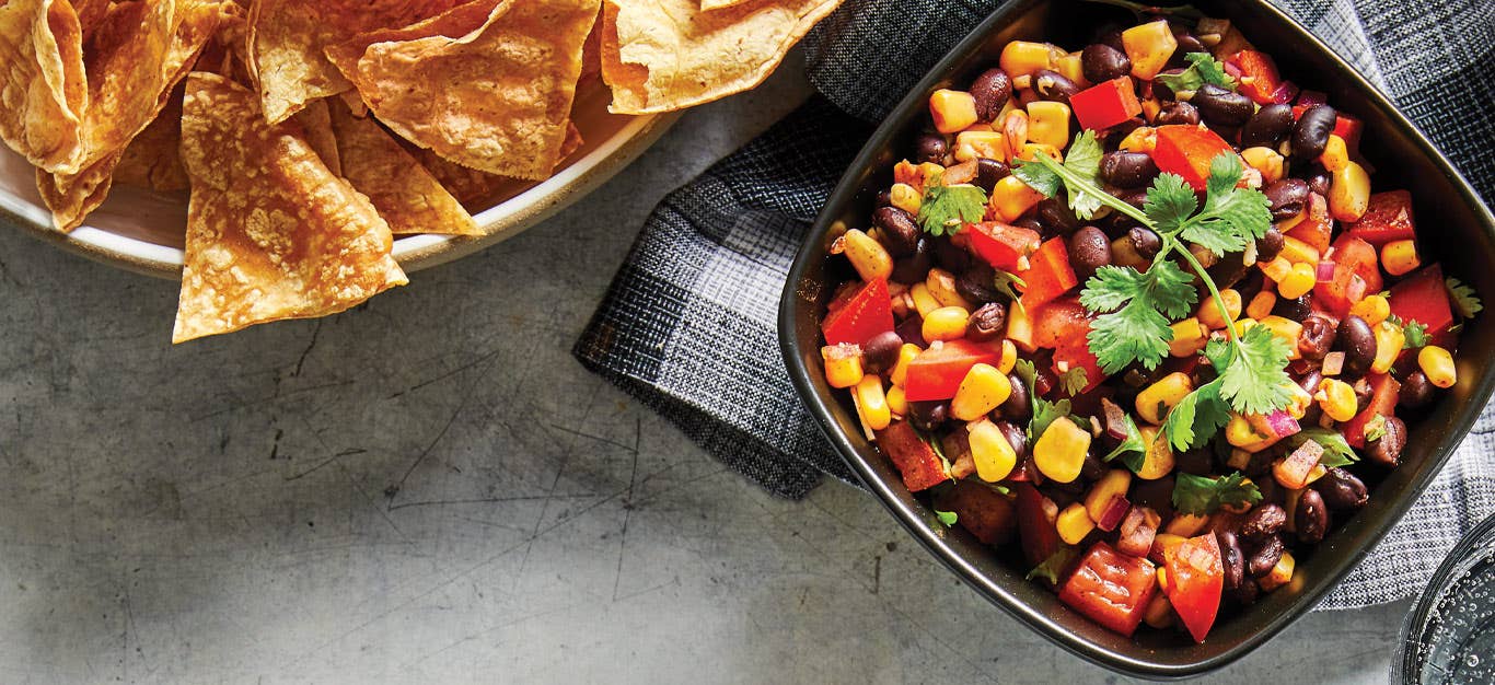 Spicy Black Bean Salsa in a black bowl with a side of tortilla chips
