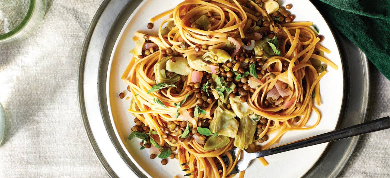 Linguine with Artichokes and Lentils on a white plate with a fork on the plate, covered in linguine