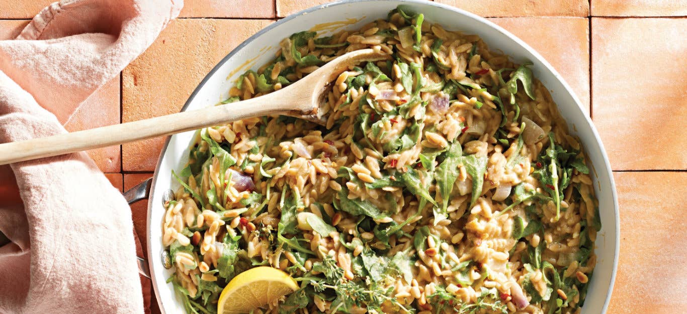 Whole Wheat Orzo and Arugula Skillet Supper in a white skillet with a wooden spoon
