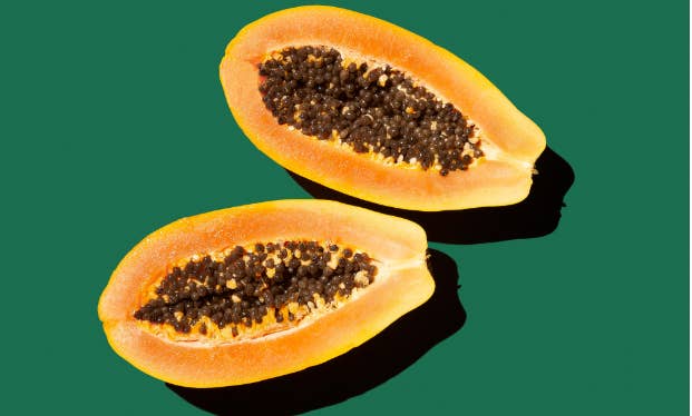 Two papaya halves with seeds, side by side on a sold green background
