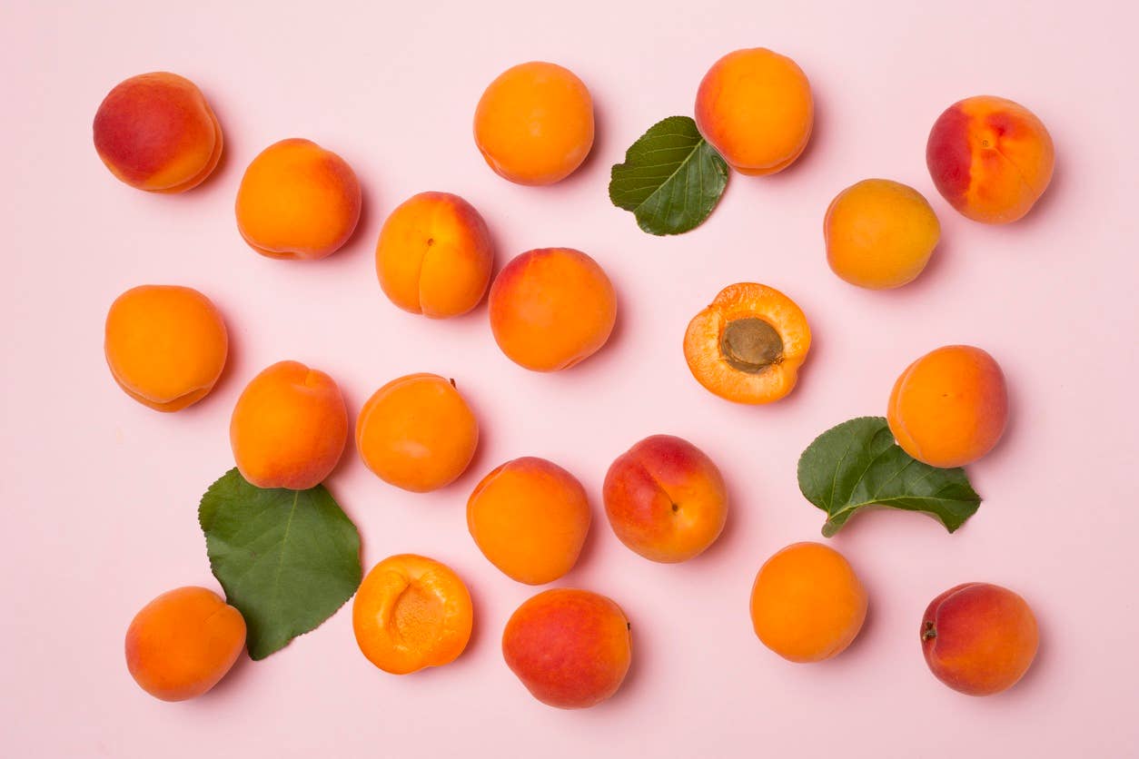 fresh orange apricots scattered across a solid pink background