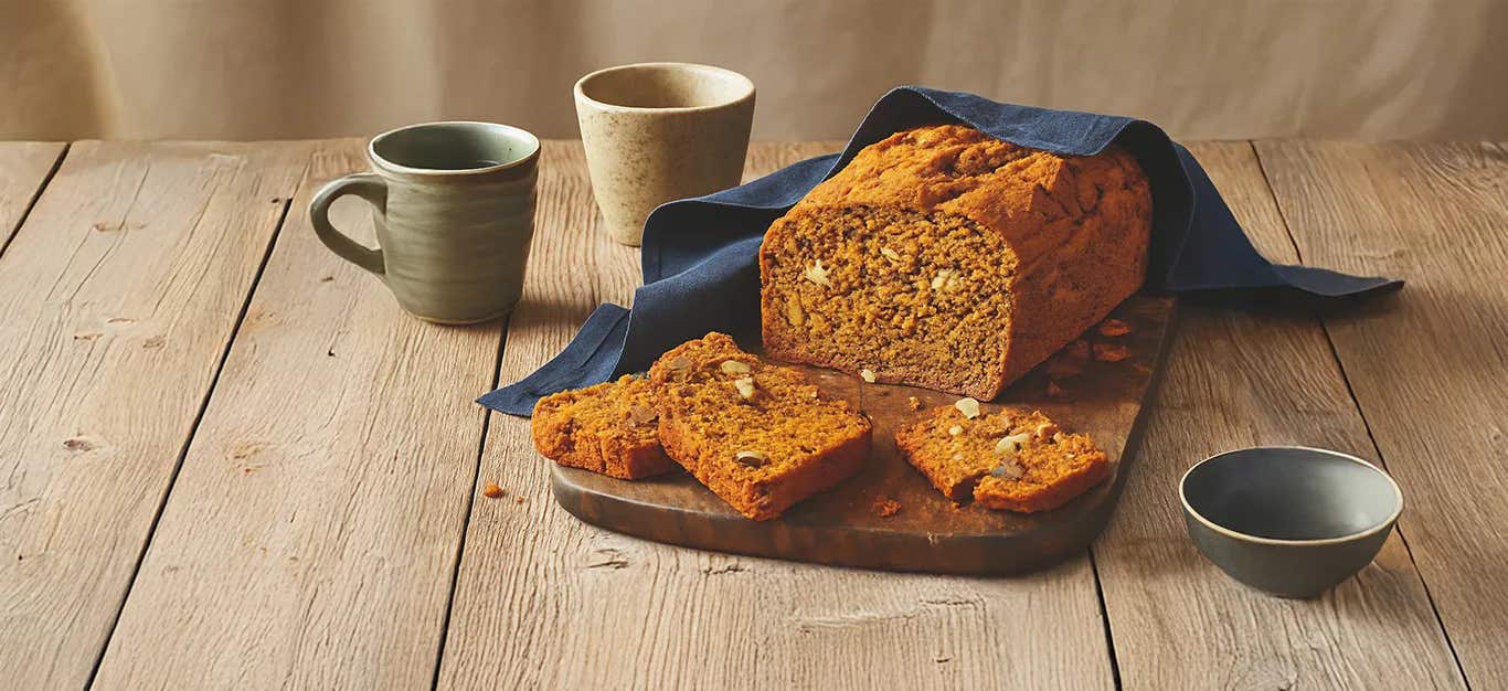 Pumpkin Spice Bread on a wooding chopping board, with a couple of slices cut, sitting in front of the loaf