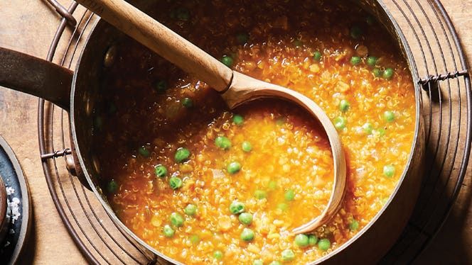 a big pot of lentil soup with quinoa and peas, and a wooden ladle sticking out