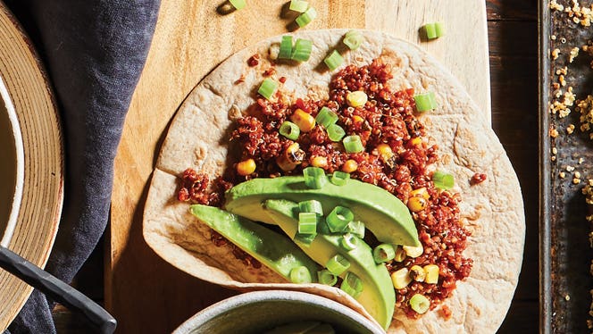 a whole wheat taco filled with vegan quinoa filling, topped with sliced avocado and scallions