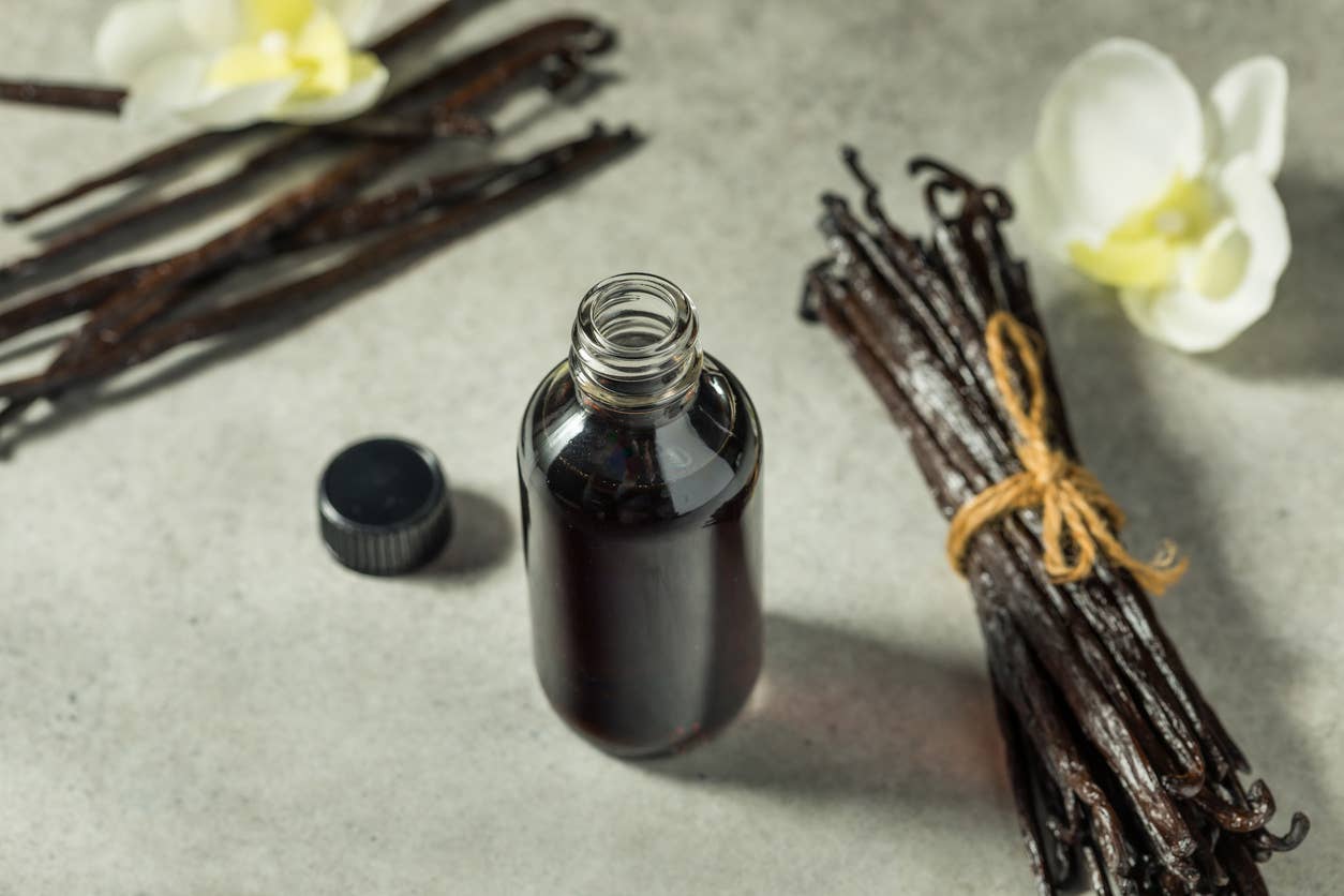 A bottle of vanilla extract beside whole vanilla bean pods and a flower