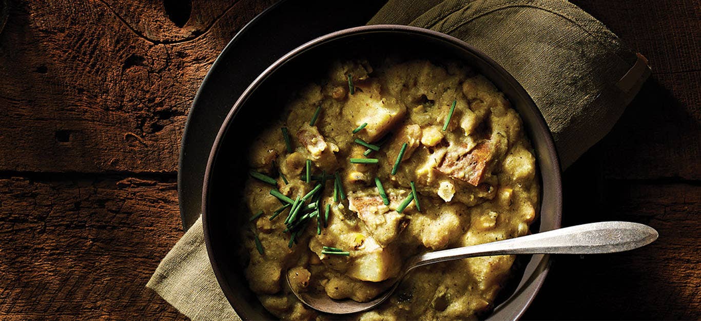 A dark grey ceramic bowl of Dairy-Free Potato Corn Chowder in a cozy, dimly lit setting