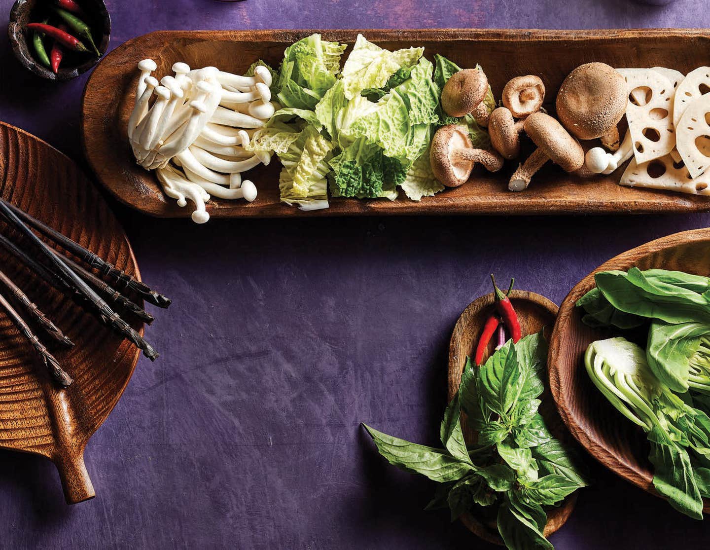 an assortment of ingredients for Vietnamese hot pot, including fresh mushrooms and greens, on a long wooden tray