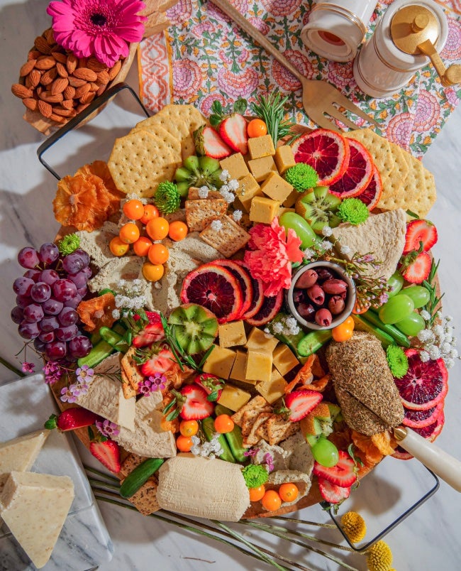 Vegan cheese board by Chef Bailey Ruskus with a colorful array of plant based ingredients including homemade vegan soft cheese and seasonal fruits and fresh herbs and edible flowers