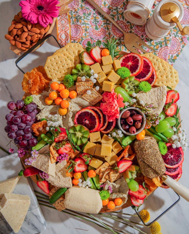 Vegan cheese board by Chef Bailey Ruskus with a colorful array of plant based ingredients including homemade vegan soft cheese and seasonal fruits and fresh herbs and edible flowers