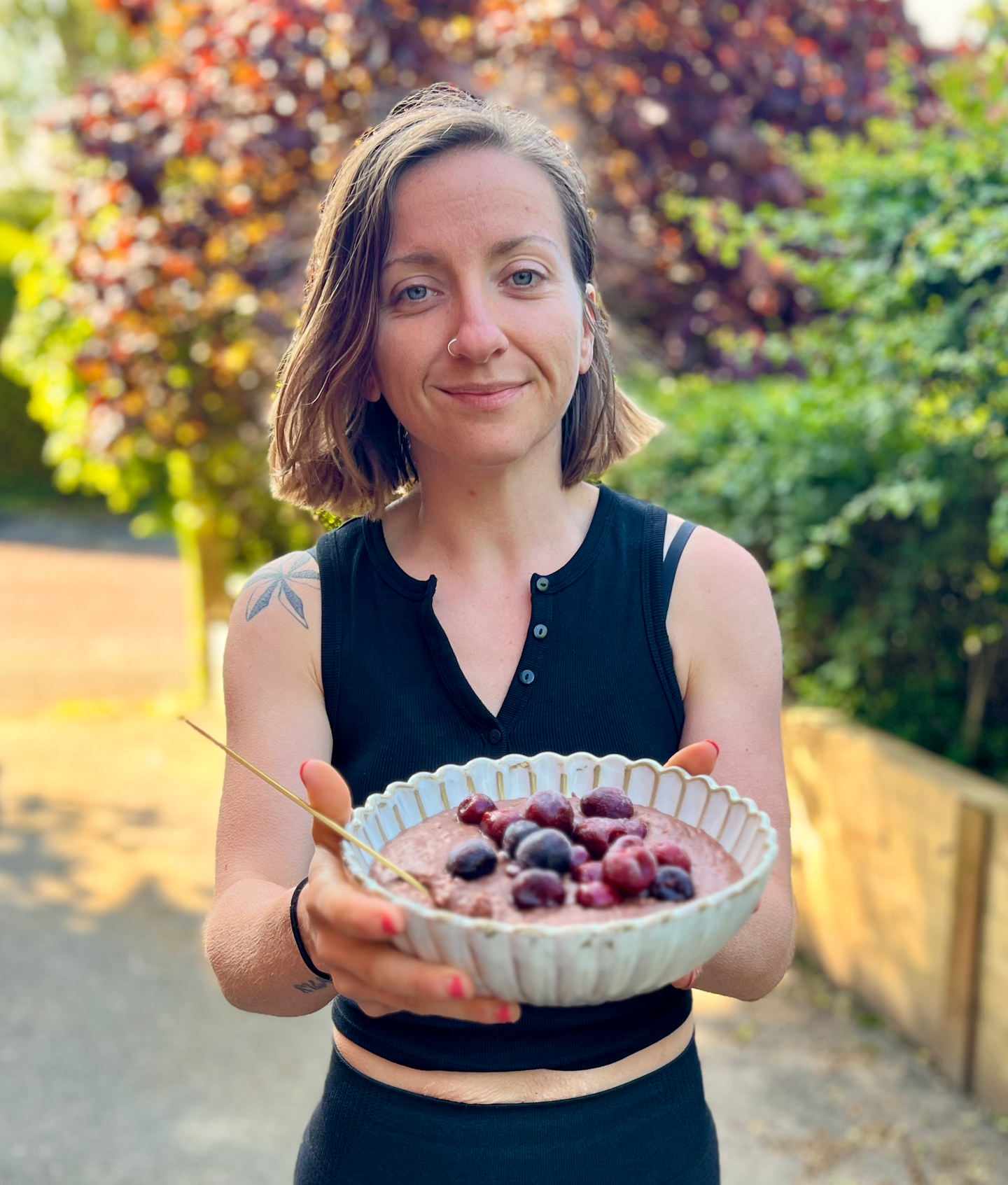 Headshot of Ami Deane aka Broccoli Mum standing outside with a bowl of fruit-topped porridge