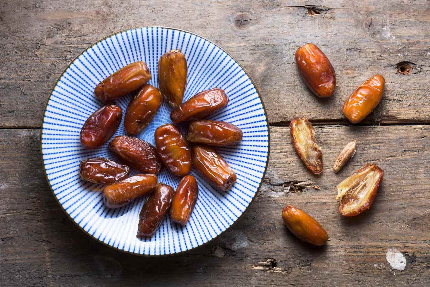dates on a wooden table, some on a blue plate and some laid directly on the table and cut open