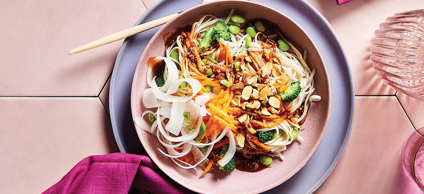 A wide-rimmed, pale pink bowl of 30-Minute Spring Roll Bowl with daikon ribbons and colorful veggies