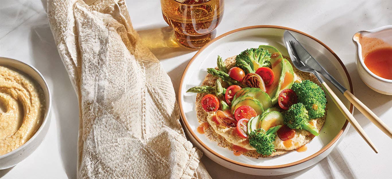 15-Minute Veggie Tostada on a plate drizzle with hot sauce next to a bowl of hummus