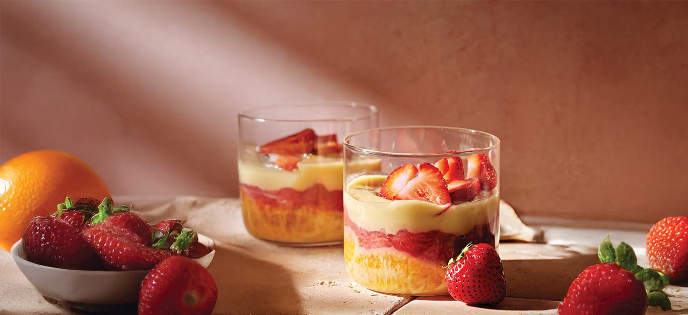 Two Strawberry-Orange Custard Cups in glass ramekins on a table with fresh strawberries and an orange