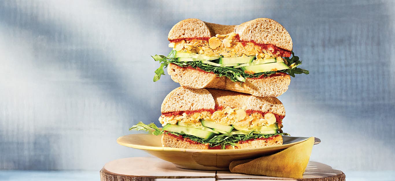 A close-up of a Sun-Dried Tomato and Chickpea Bagel Sandwich cut in half and stacked on a plate