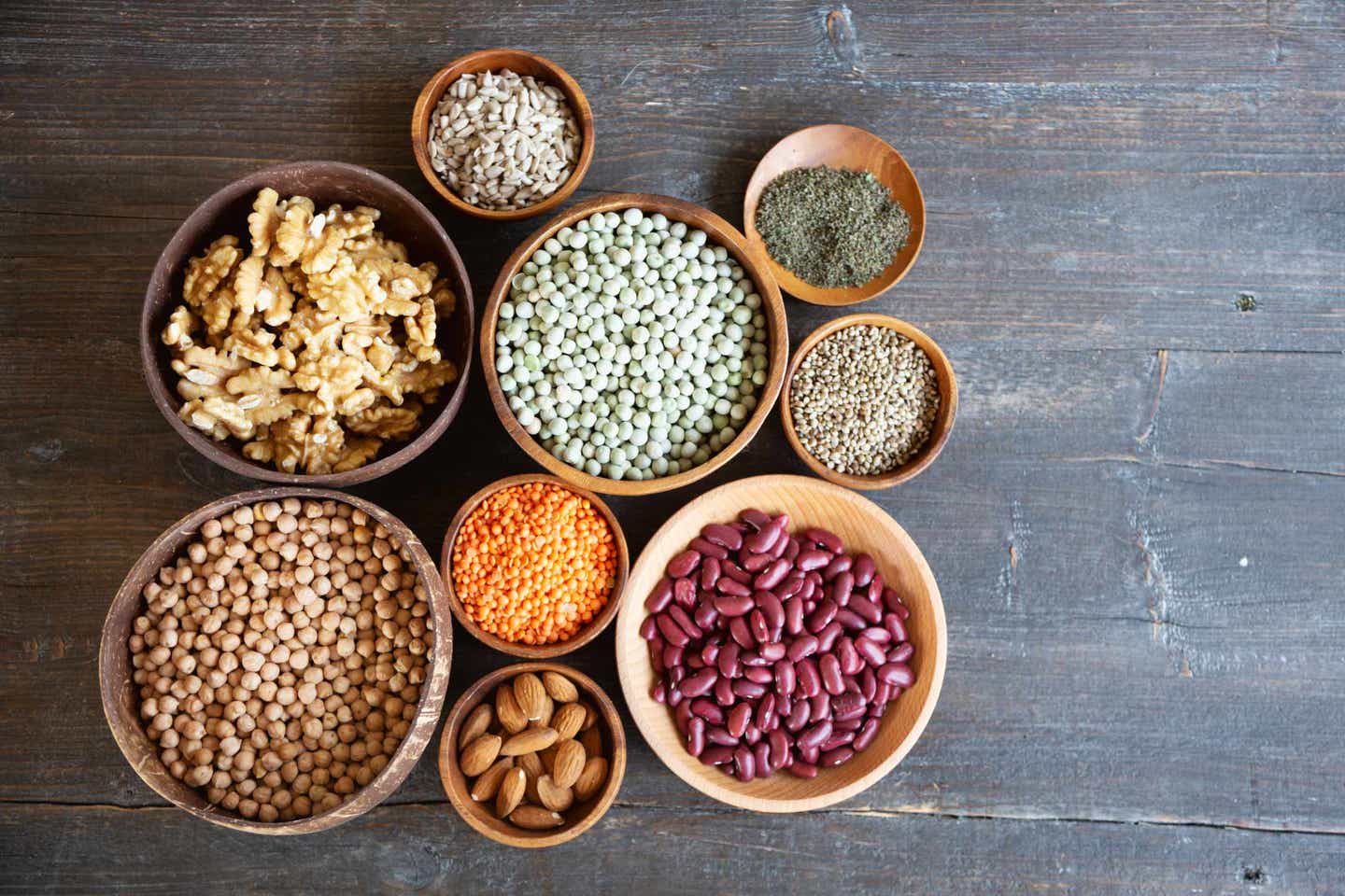 beans-and-nuts A collection of small and medium size bowls, each filled with legumes or nuts, on a wooden gray background